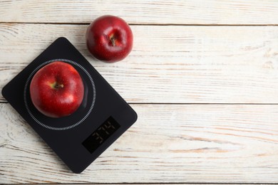 Photo of Ripe red apples and electronic scales on white wooden table, flat lay. Space for text
