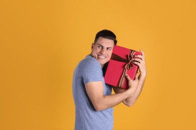 Photo of Greedy man hiding gift box on yellow background, space for text