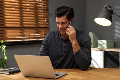 Man with modern smartphone and laptop at wooden table in office. Searching information