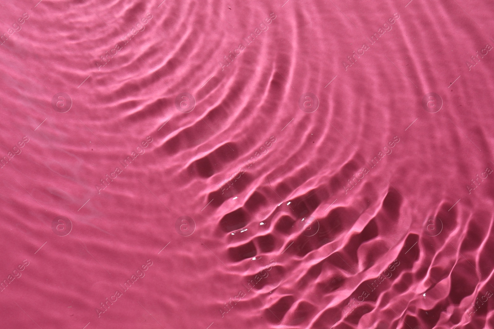 Photo of Rippled surface of clear water on bright pink background, top view
