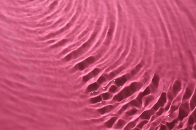 Rippled surface of clear water on bright pink background, top view