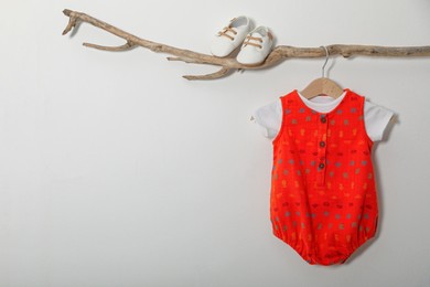 Photo of Baby bodysuit and booties on decorative branch near light grey wall. Space for text