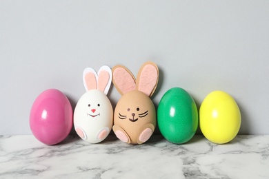 Two eggs as cute bunnies among others on white marble table against light grey background. Easter celebration