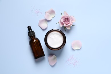 Bottle of cosmetic serum, cream, flower and petals on light blue background, flat lay