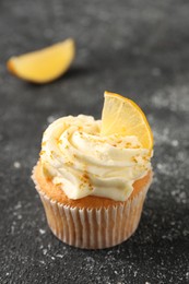 Tasty cupcake with cream, zest and lemon slice on black textured table, closeup