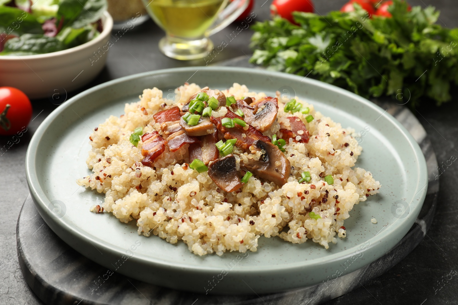 Photo of Plate of tasty quinoa porridge with fried bacon, mushrooms and green onion on black table, closeup