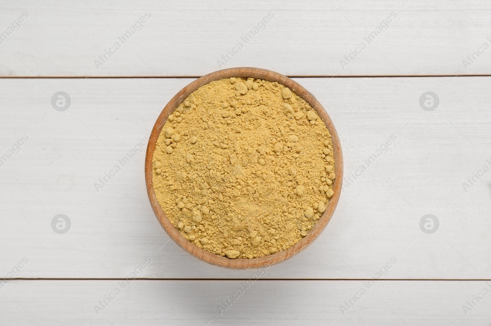 Photo of Bowl of aromatic mustard powder on white wooden table, top view