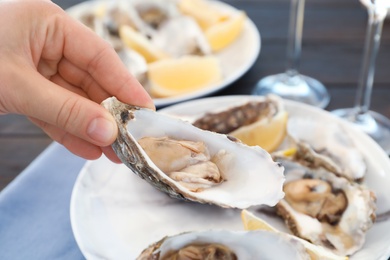 Woman with fresh oyster over plate, focus on hand