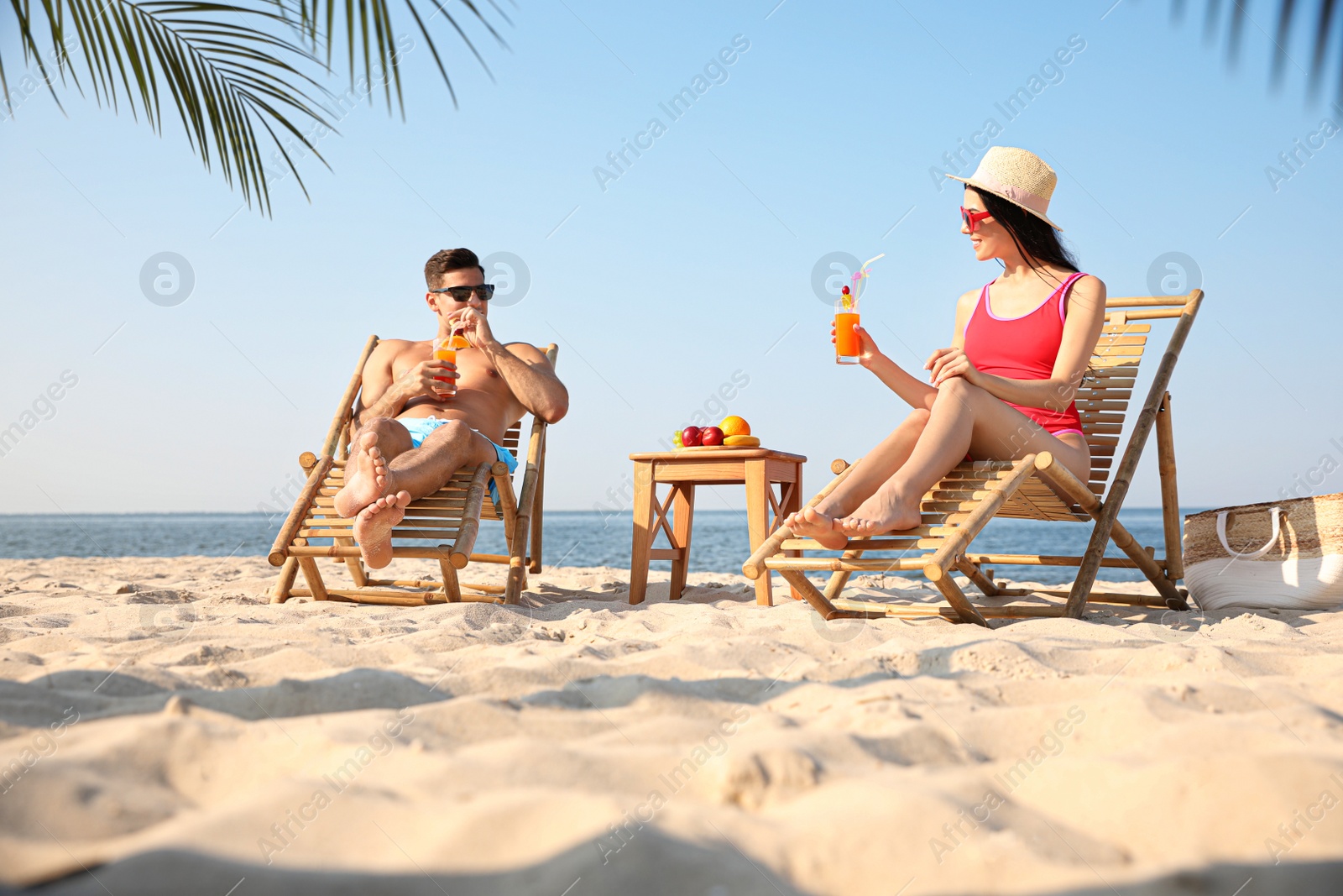 Photo of Couple with drinks resting on sunny beach at resort