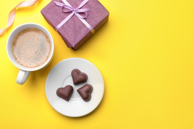 Cup of coffee, chocolate candies and gift box on yellow background, flat lay with space for text. Valentine's day breakfast
