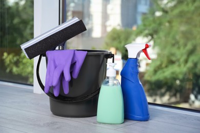 Photo of Cleaning supplies and black bucket with tools on window sill indoors