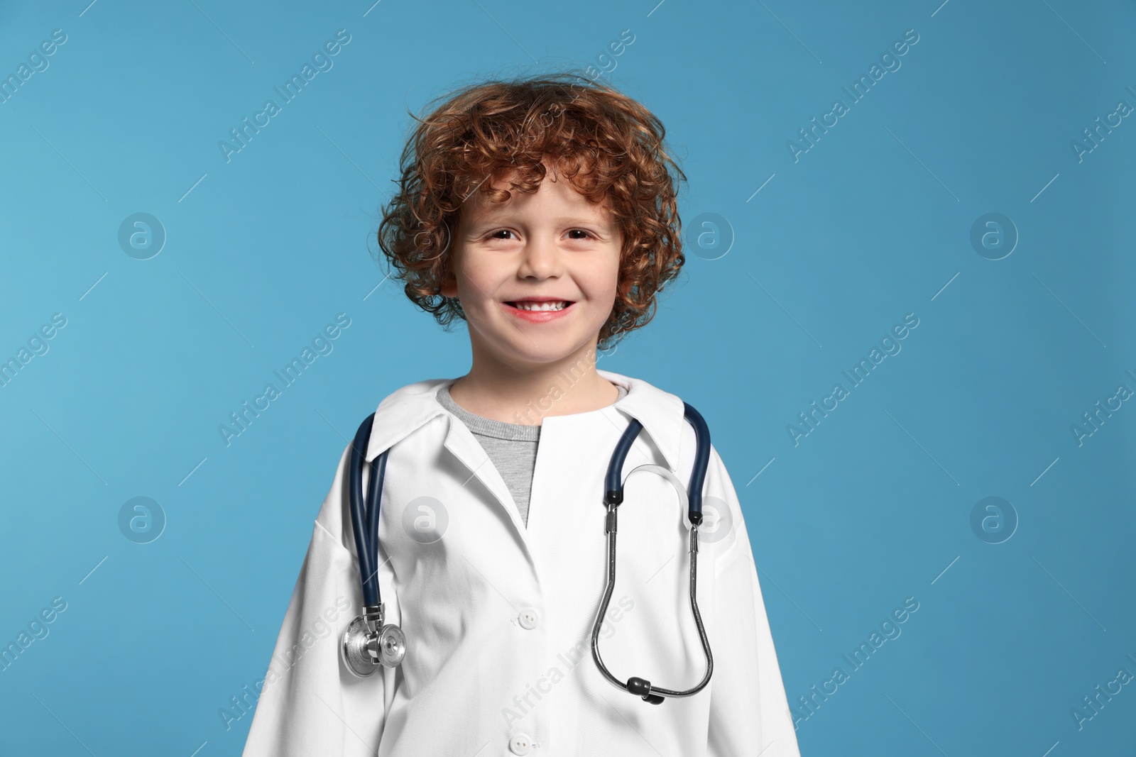 Photo of Little boy in medical uniform with stethoscope on light blue background