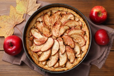 Photo of Delicious apple pie, fresh fruits and dry leaves on wooden table, flat lay