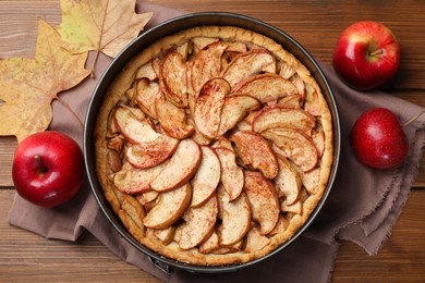 Delicious apple pie, fresh fruits and dry leaves on wooden table, flat lay