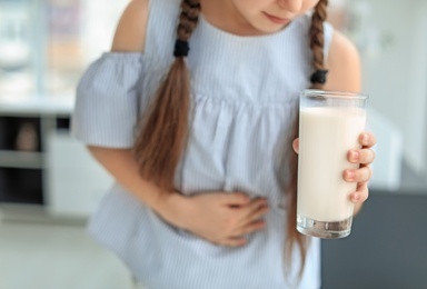 Photo of Little girl with dairy allergy holding glass of milk indoors