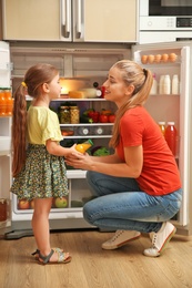 Young mother and daughter with juice near refrigerator at home