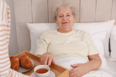 Photo of Young caregiver serving breakfast for senior woman in bedroom. Home care service