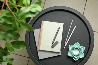 Notebooks, pen, pencils and decor on round table indoors, top view