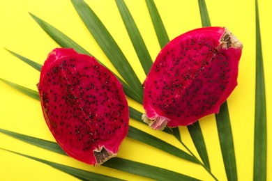 Photo of Delicious cut red pitahaya fruit with palm leaf on yellow background, flat lay