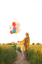 Photo of Young woman and her daughter with colorful balloons outdoors on sunny day