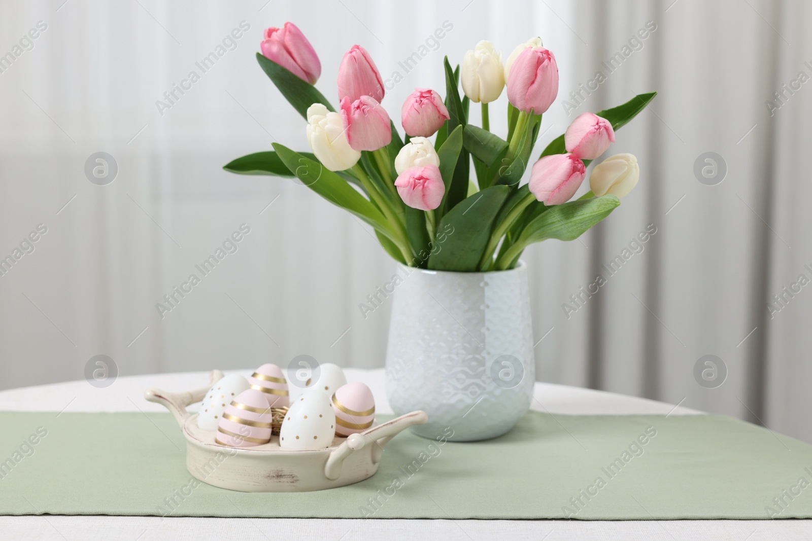 Photo of Easter decorations. Bouquet of tulips and painted eggs on white table indoors