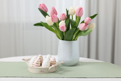 Easter decorations. Bouquet of tulips and painted eggs on white table indoors