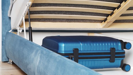 Storage drawer under bed with blue suitcase indoors
