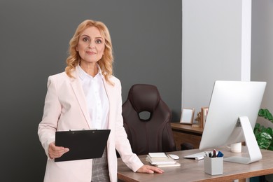 Photo of Happy lady boss with clipboard near desk in office. Successful businesswoman