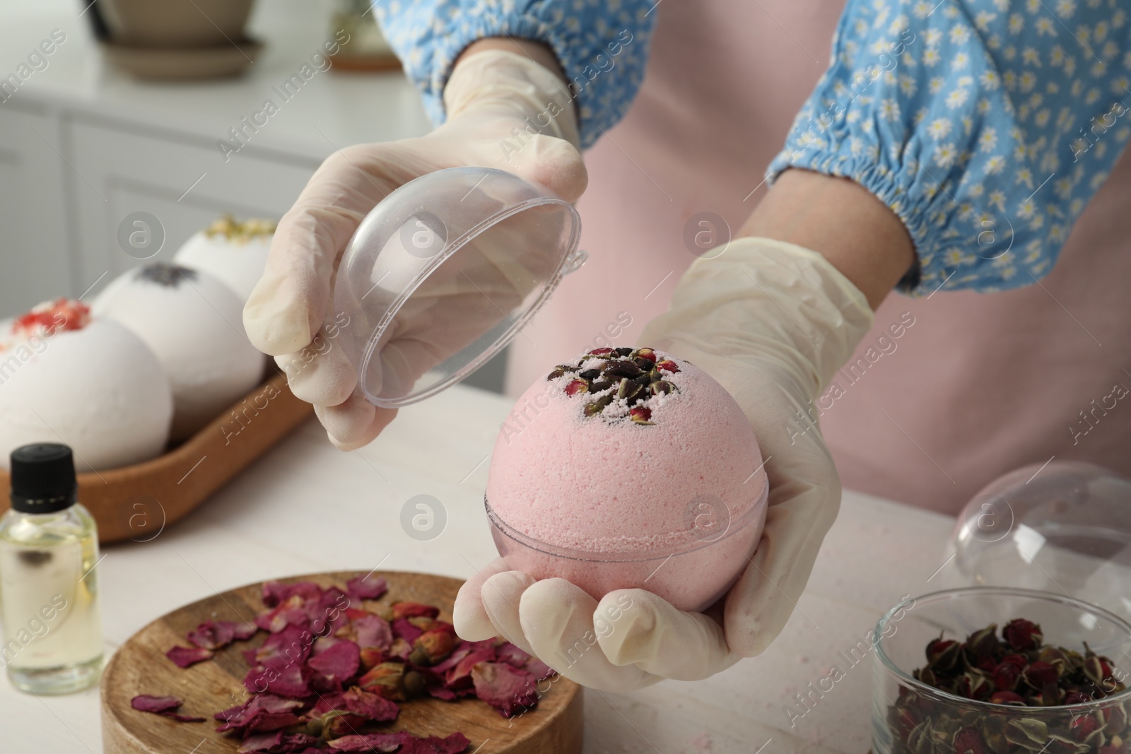 Photo of Woman in gloves with self made bath bomb at white table indoors, closeup