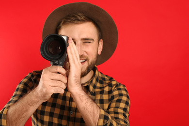 Young man using vintage video camera on red background, focus on lens