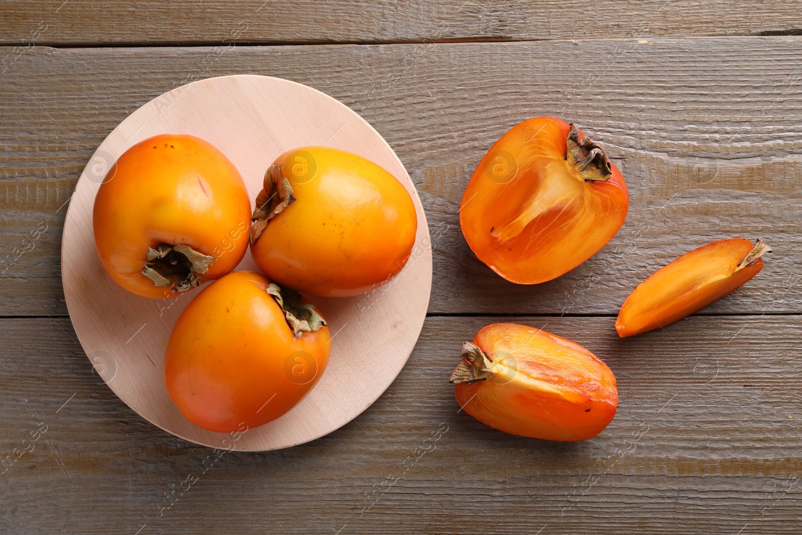 Photo of Whole and cut delicious ripe persimmons on wooden table, flat lay