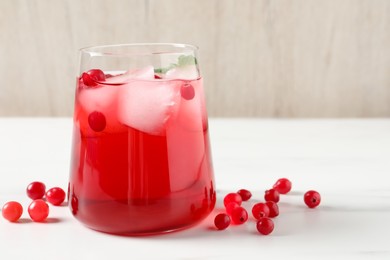 Photo of Tasty cranberry juice with ice cubes in glass and fresh berries on white wooden table, closeup. Space for text