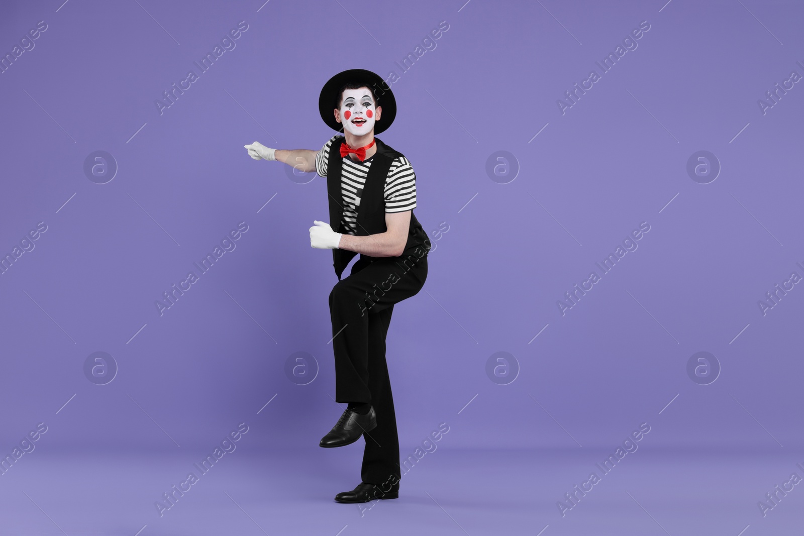 Photo of Funny mime artist in hat posing on purple background