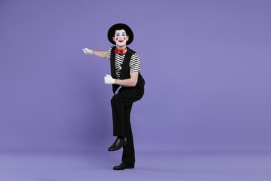 Photo of Funny mime artist in hat posing on purple background