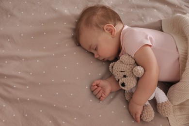 Photo of Adorable little baby with toy bear sleeping on bed, above view. Space for text