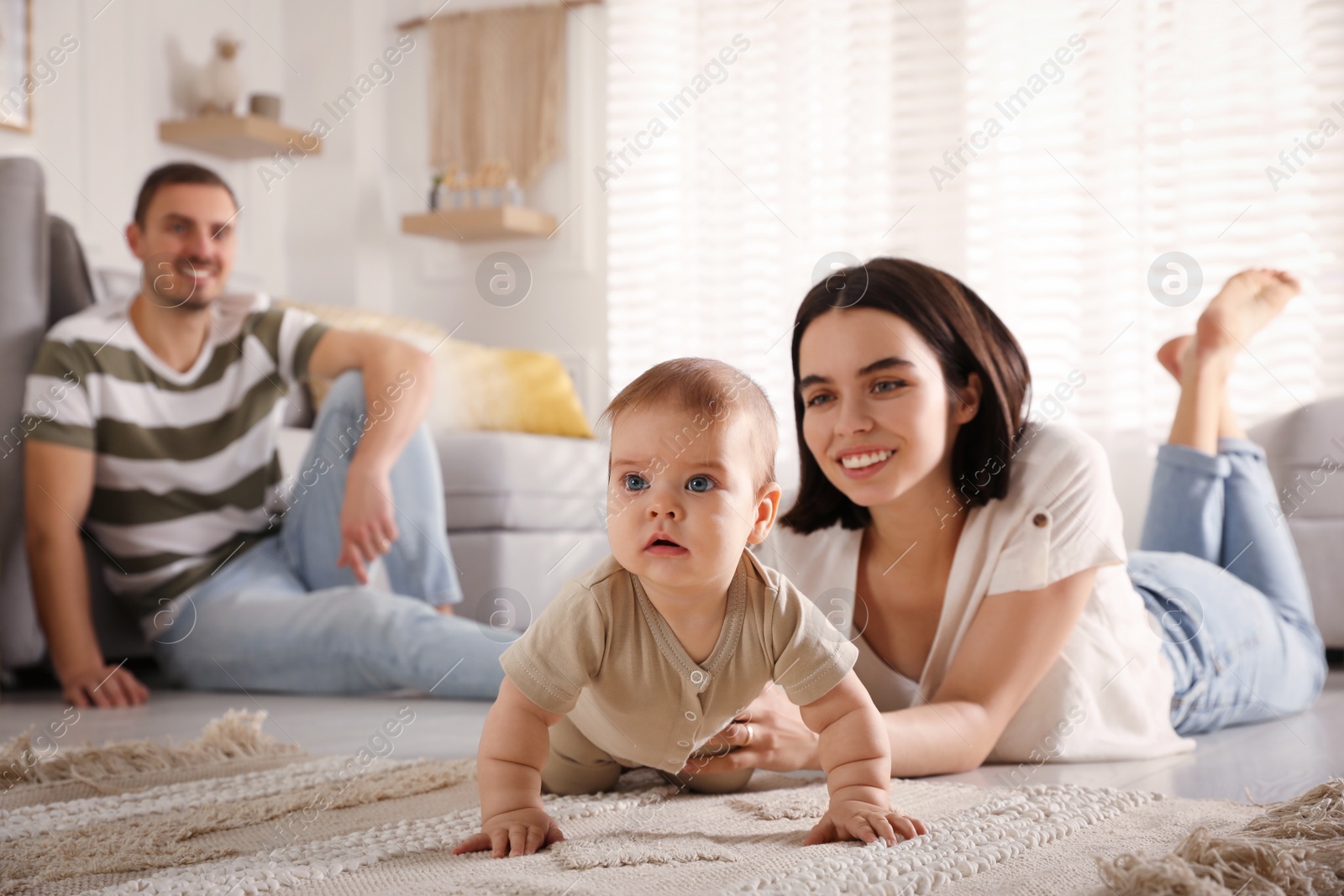 Photo of Happy parents helping their cute baby to crawl on floor at home