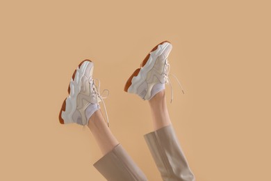 Photo of Woman wearing pair of new stylish sneakers on beige background, closeup