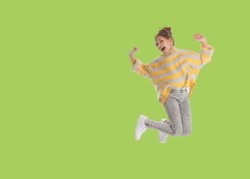 Cute girl jumping on light green background, space for text