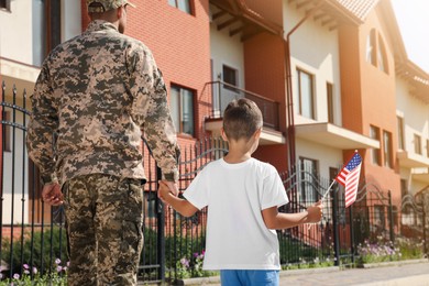 Photo of Soldier and his little son with American flag outdoors, back view. Veterans Day in USA