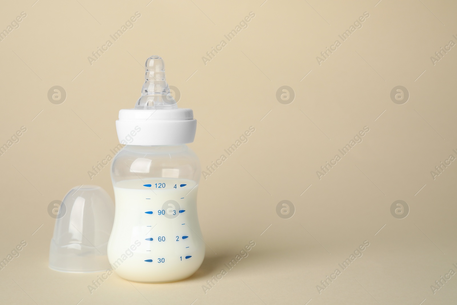 Photo of Feeding bottle with infant formula on beige background. Space for text