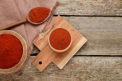 Bowls and spoon with aromatic paprika powder on old wooden table, flat lay. Space for text