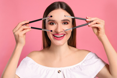 Photo of Beauty blogger with makeup brushes on pink background