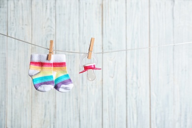 Baby socks and pacifier on laundry line against wooden background, space for text. Child accessories