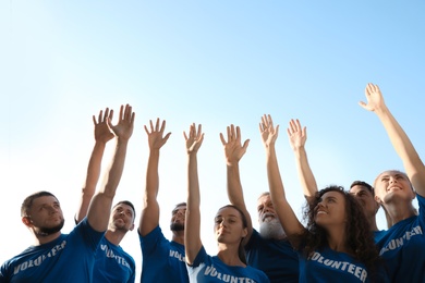 Photo of Group of volunteers raising hands outdoors on sunny day