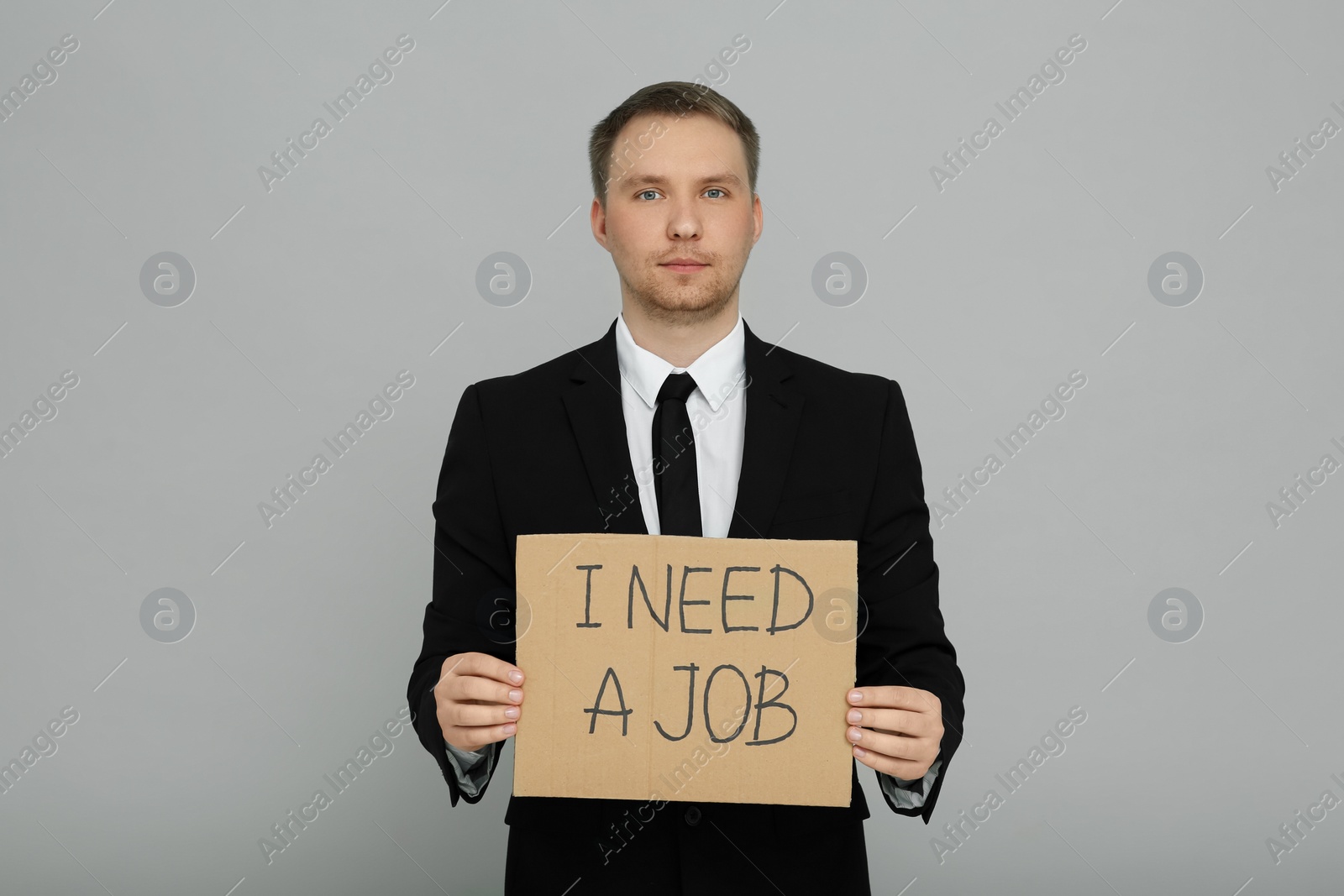 Photo of Unemployed man holding sign with phrase I Need A Job on light grey background