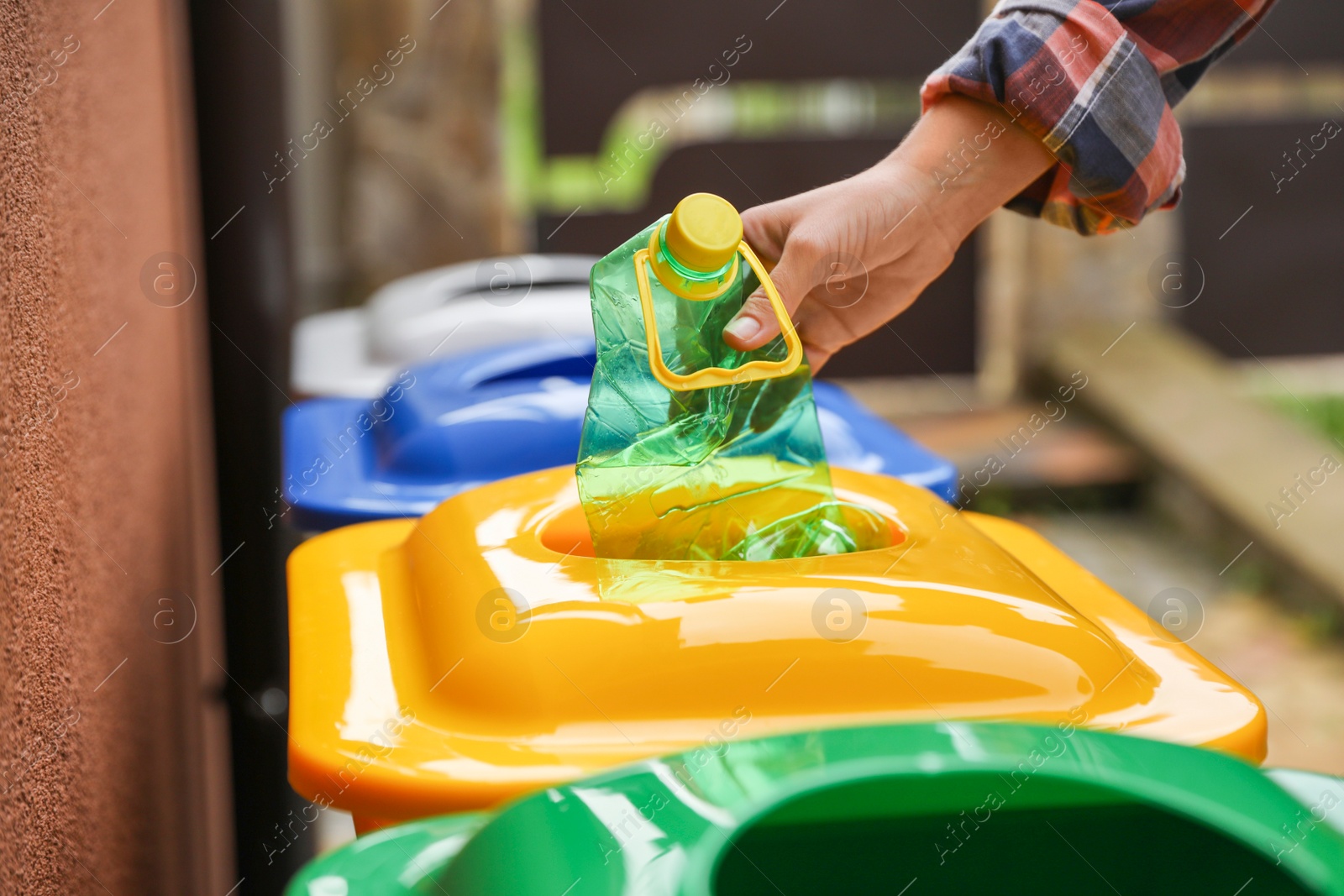 Photo of Woman throwing plastic bottle into recycling bin outdoors, closeup