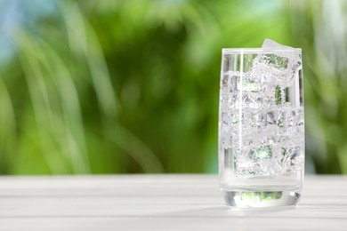 Photo of Glass of refreshing soda water with ice cubes on white table outdoors, space for text