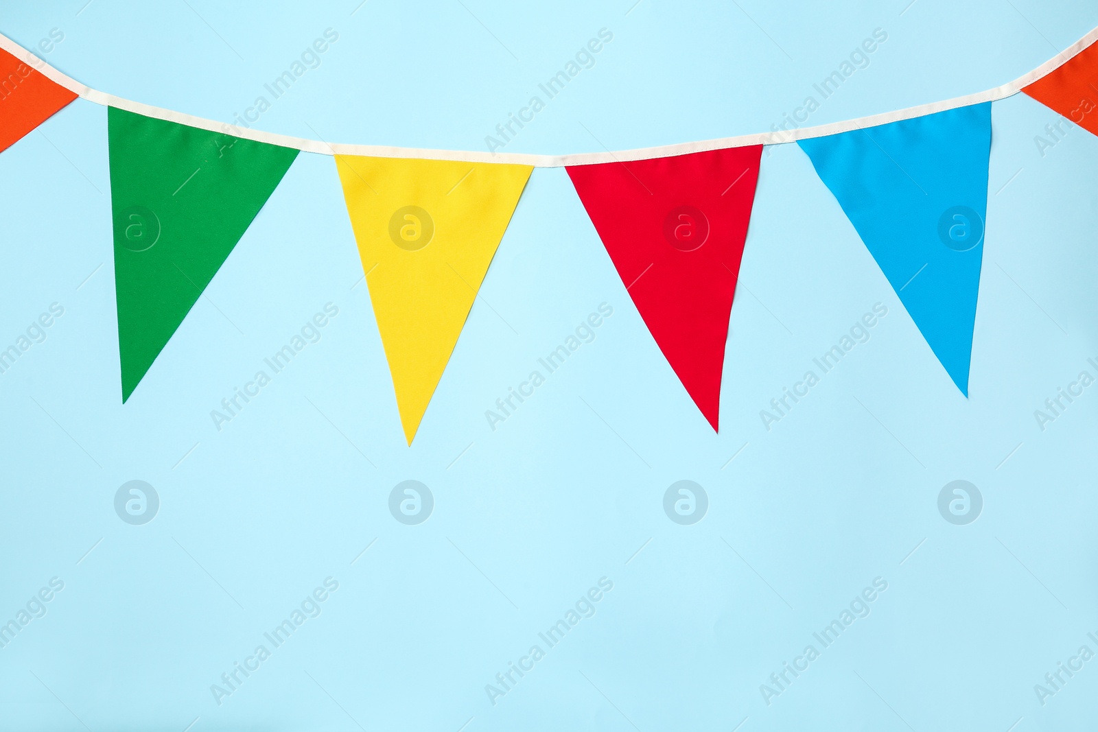 Photo of Bunting with colorful triangular flags on light blue background. Space for text
