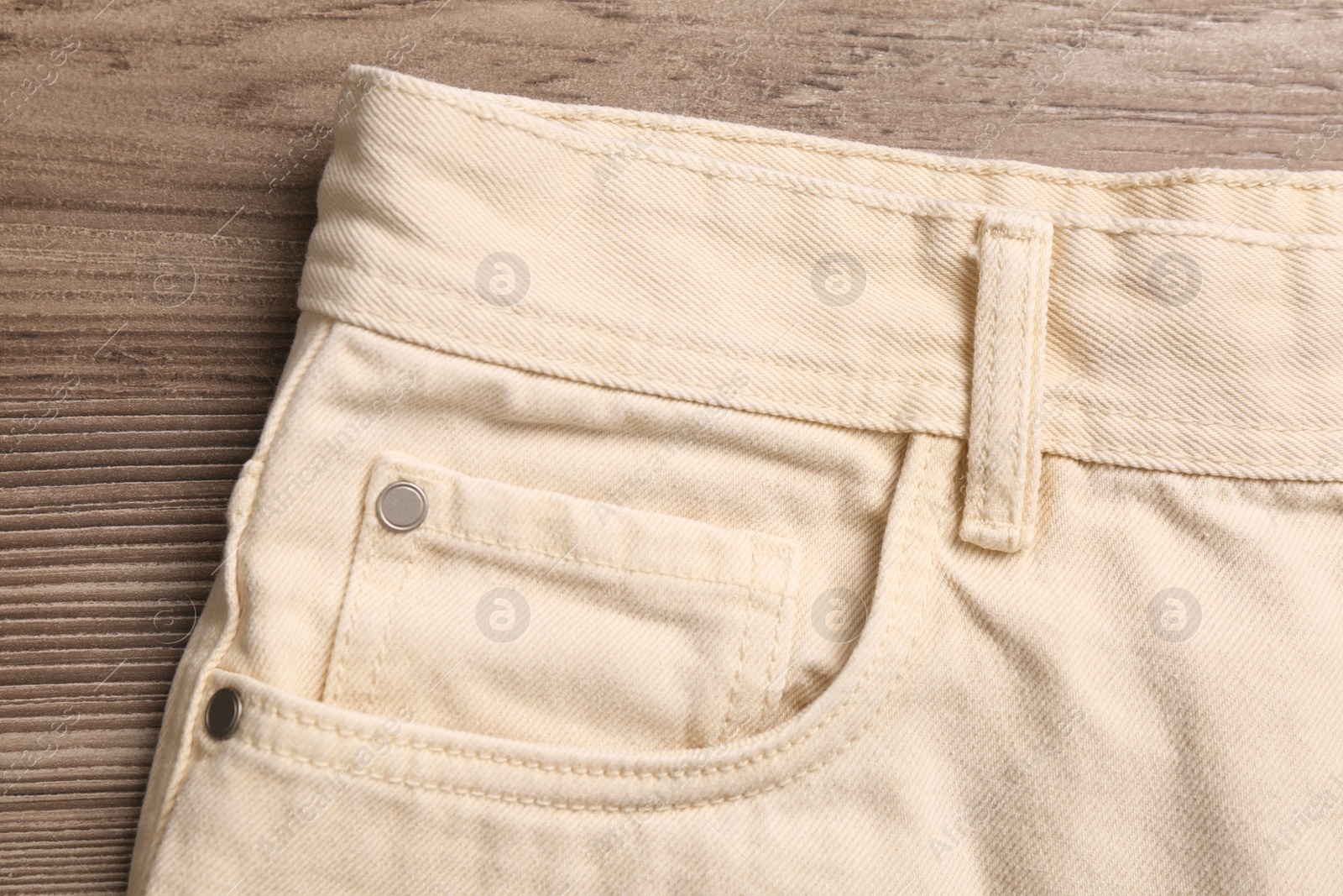 Photo of Stylish beige  jeans on wooden background, closeup of inset pocket