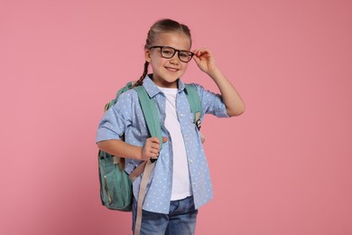 Photo of Happy schoolgirl in glasses with backpack on pink background